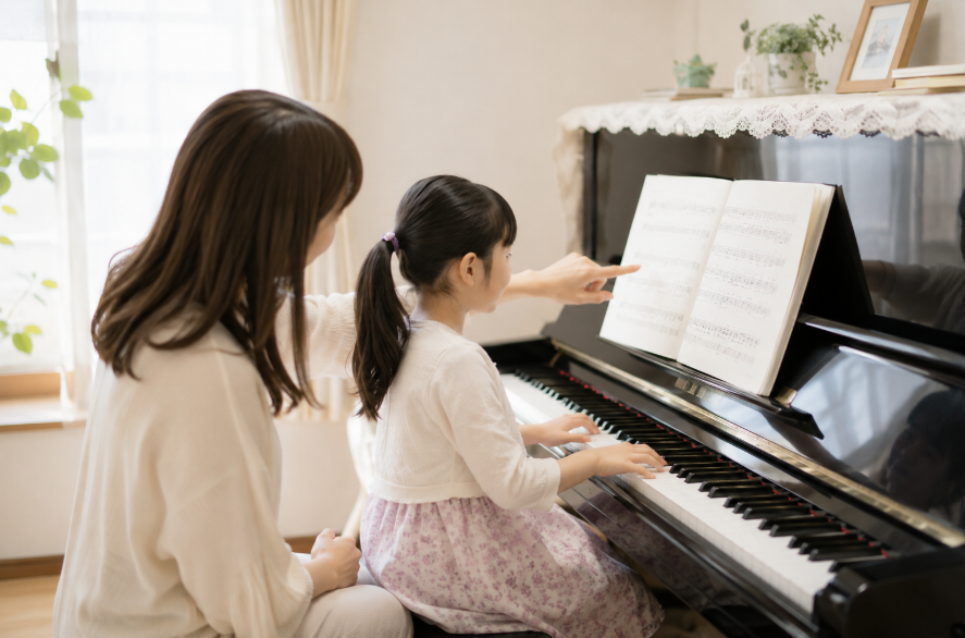 先生が娘さんの隣に座り、楽譜を指しながら教える様子